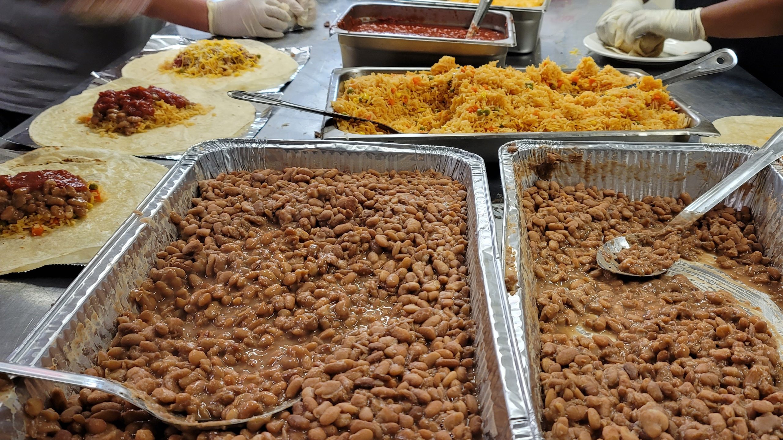 Trays of pinto beans and Mexican rice prepared for burrito assembly